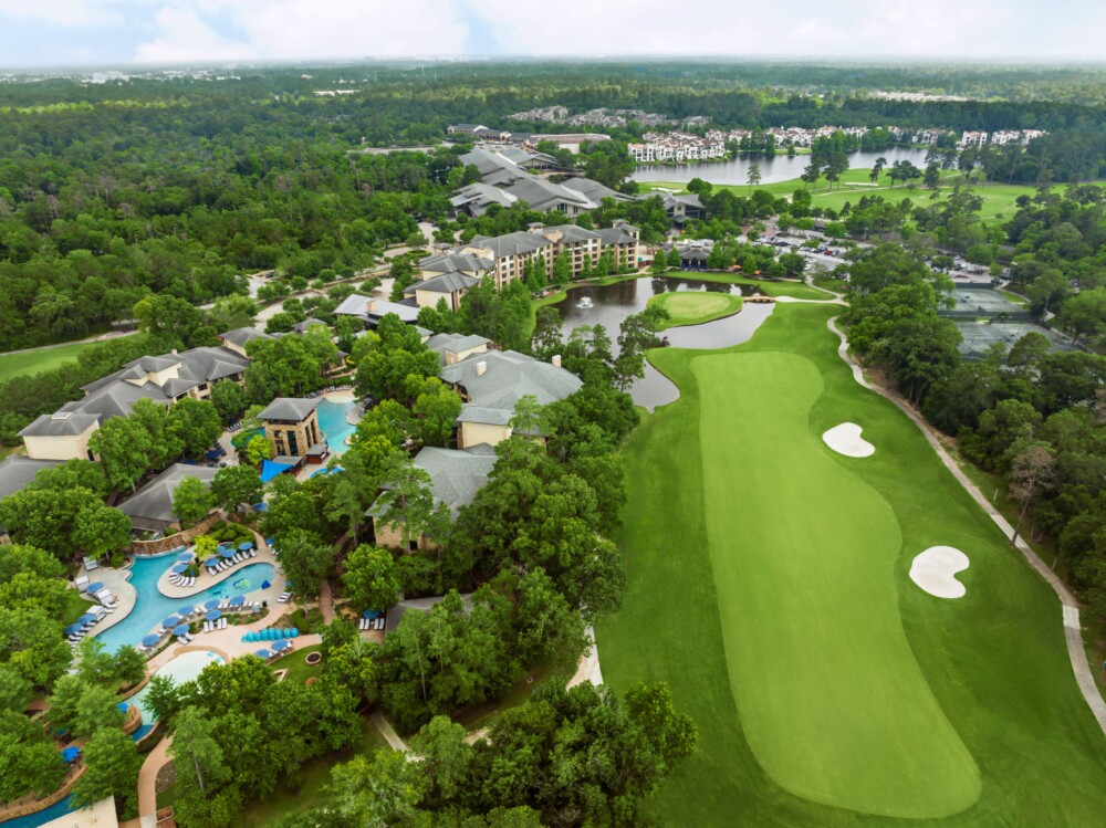 Aerial view of the resort showing the hotel, pool, golf course, ponds, tennis courts and surrounding trees.