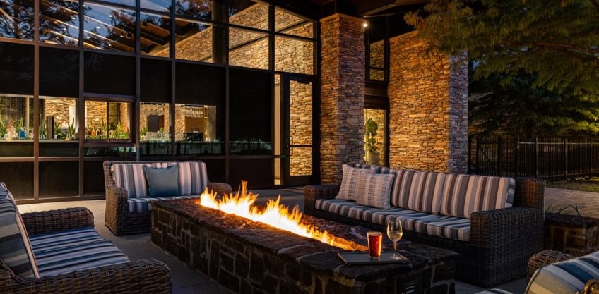 Outdoor patio area at night. Chairs and benches surround a rectangle gas firepit.